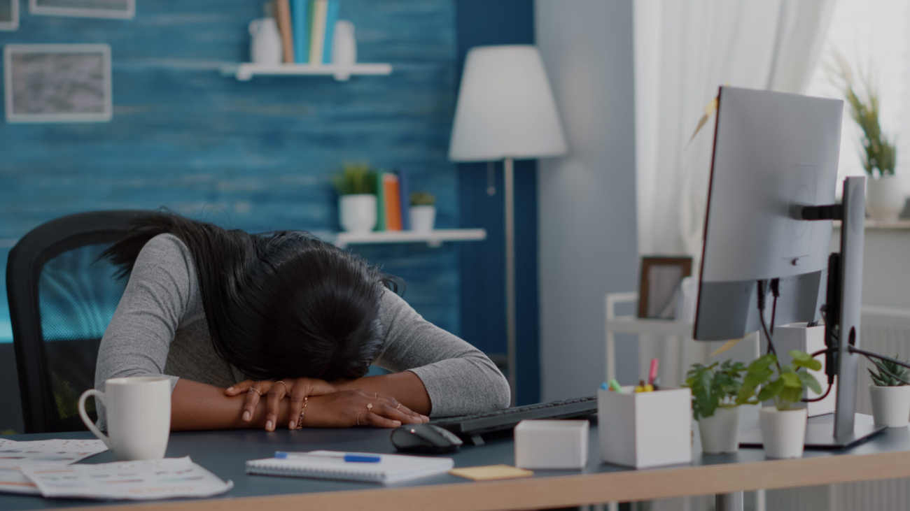 Disappointed workaholic student sleeeping on desk table in living room after working remote from home at job project deadline. Workaholic exhausted young african american woman searching online business course